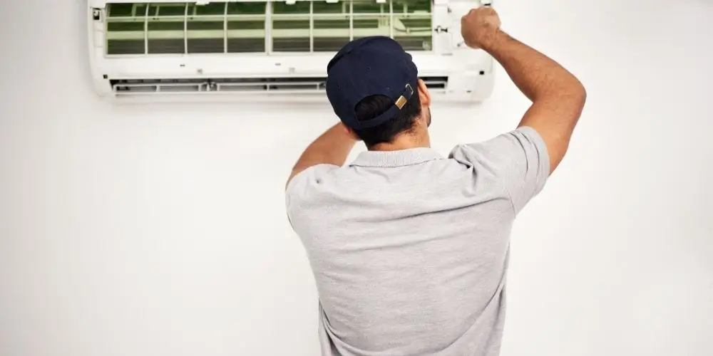 A professional AC specialist repairing a residential air conditioning unit with tools.